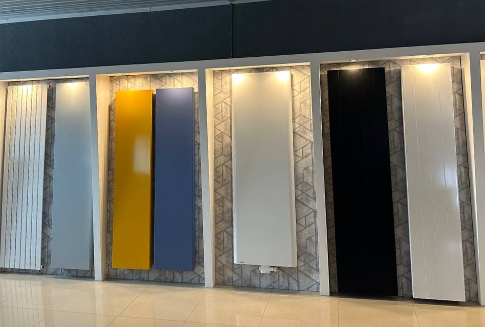 Шоурум с вертикальными высокими радиаторами, панельный радиатор, плоские радиаторы белого цвета, панельные радиаторы в желтом и голубом, плоские вертикальные профили, соединенные двумя круглыми коллекторами в черном и белом цветах